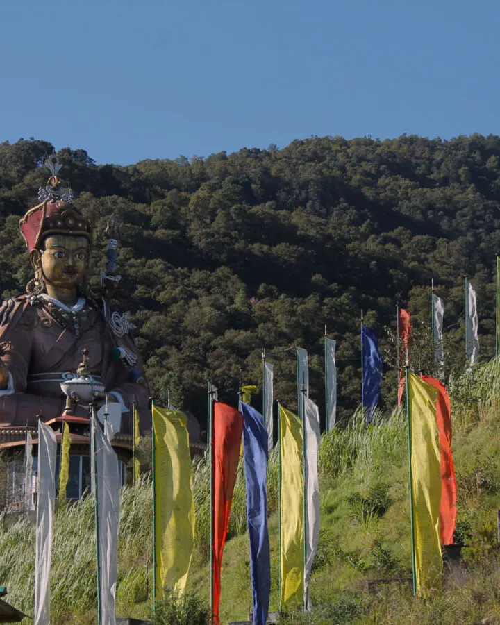 Colourful prayer flags beside a statue on a Bhutanese hillside