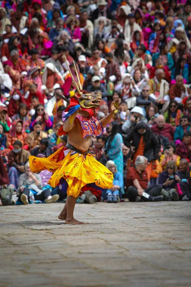 Mask dancer in a yellow costume spinning at a tshechu