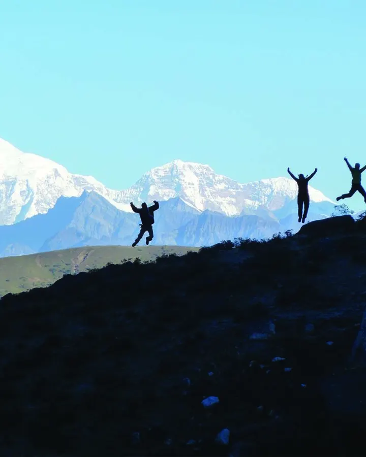 Trekkers celebrating on a ridge with snow peaks behind